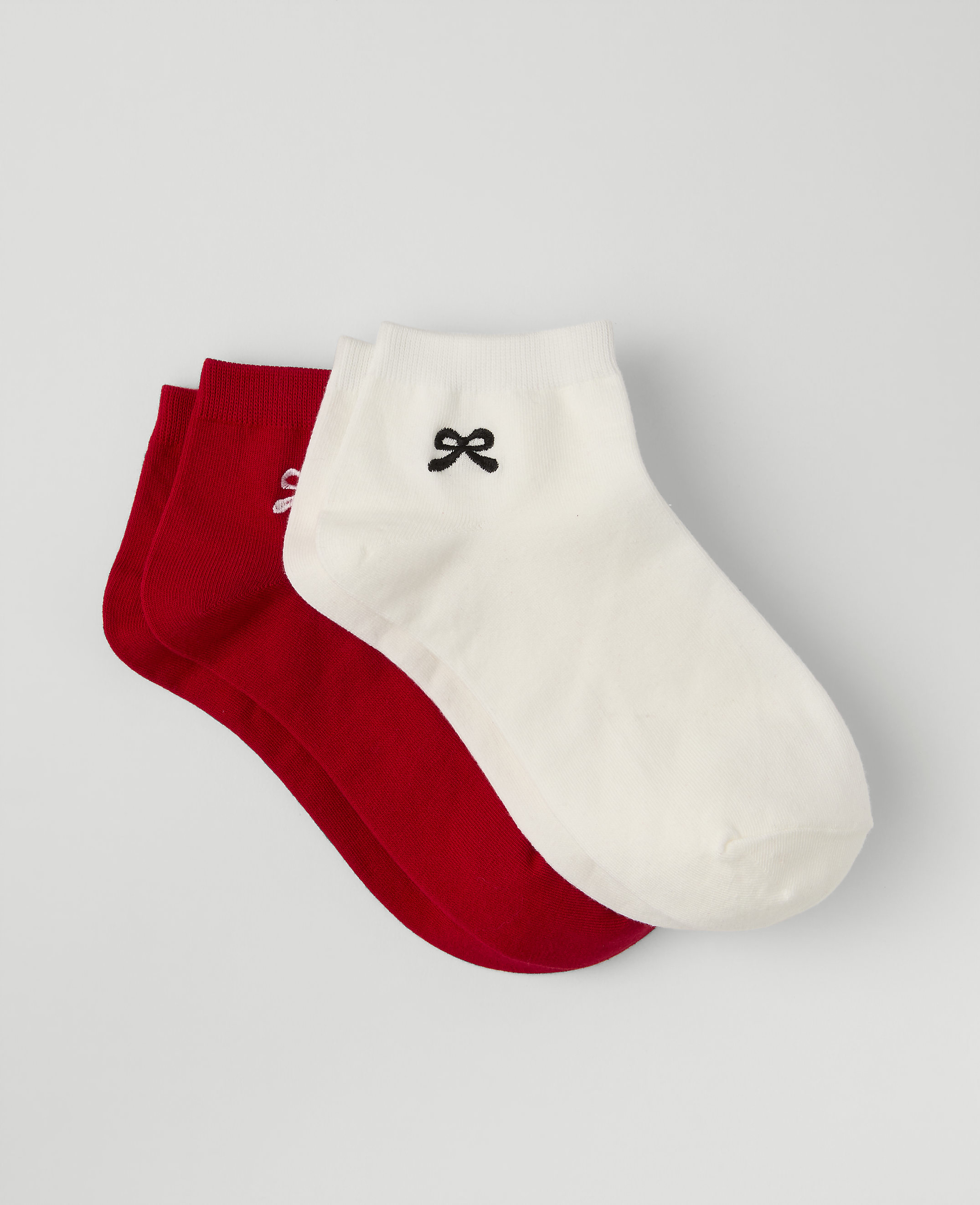 Three pairs of socks, one white with a small black bow and two red, are stacked against a plain light gray background.