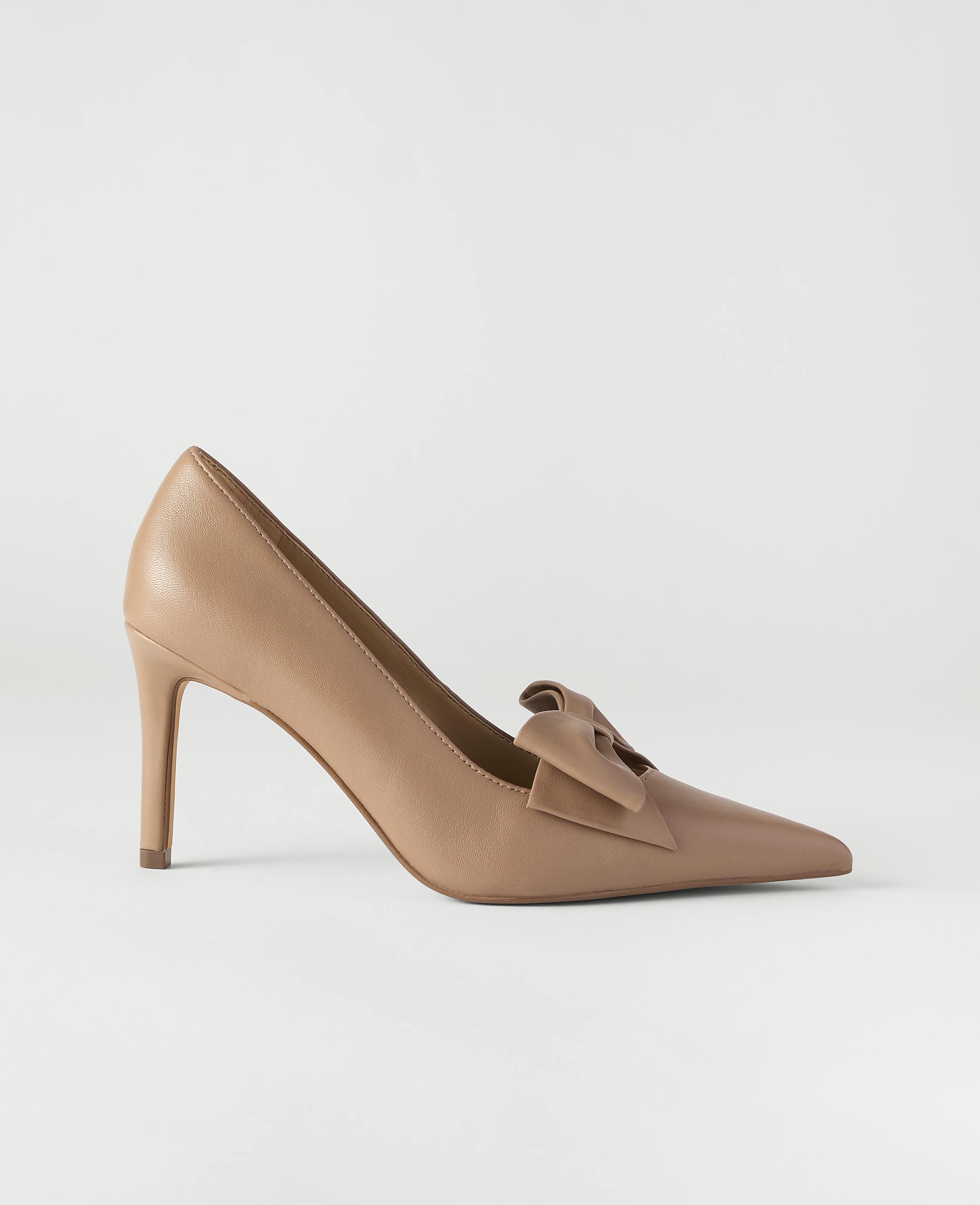 A tan pointed-toe pump with a bow detail sits centered against a plain, light gray background.