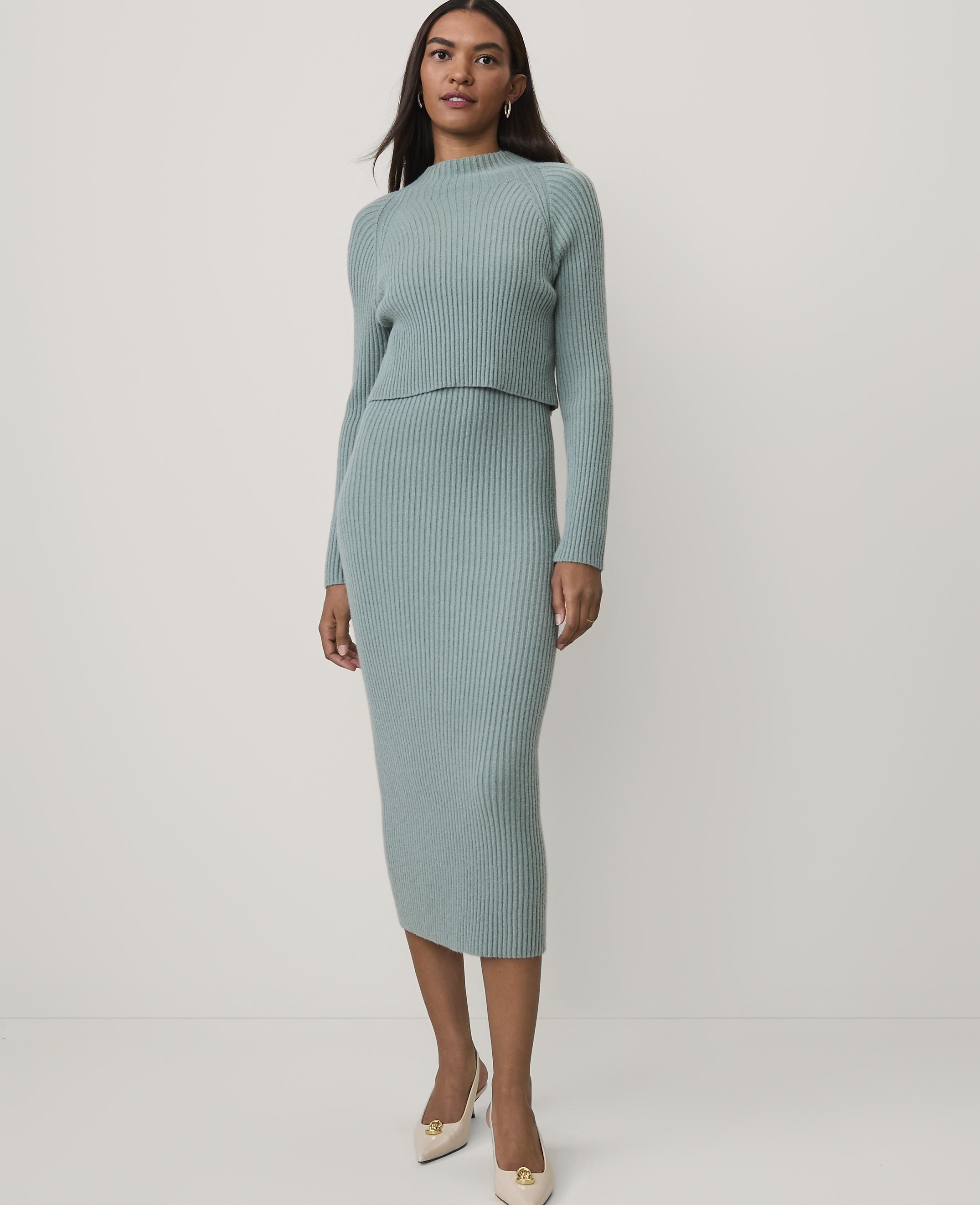 A woman wearing a light blue ribbed knit two-piece set and beige heels stands against a plain white background.