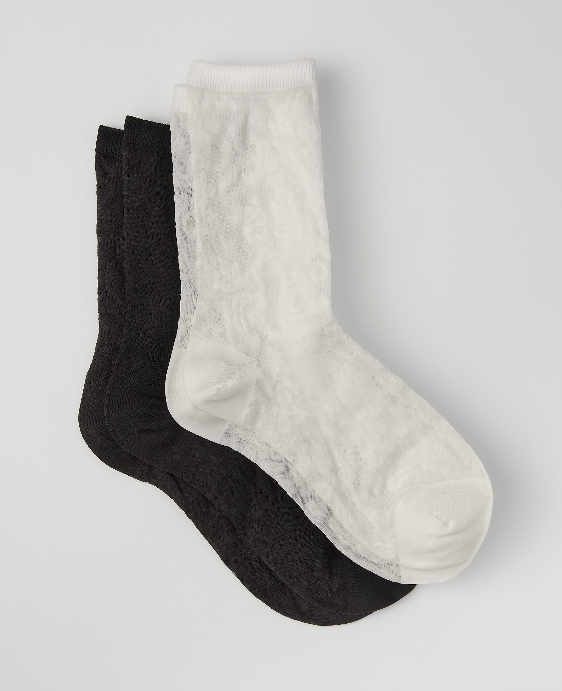 A white sock rests on top of two black socks against a plain light gray background.