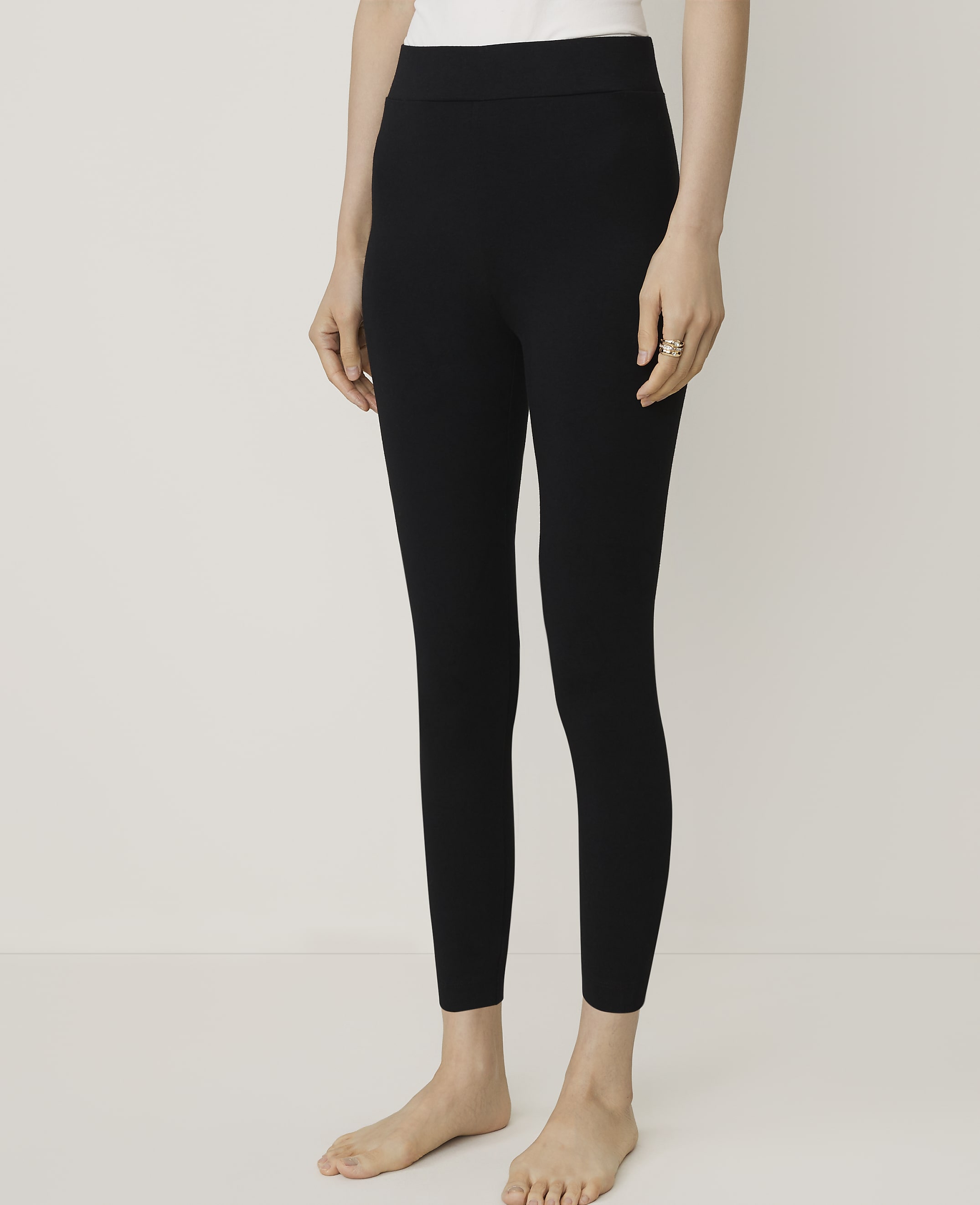 A person wearing black leggings and a white top stands against a plain, light-colored background.