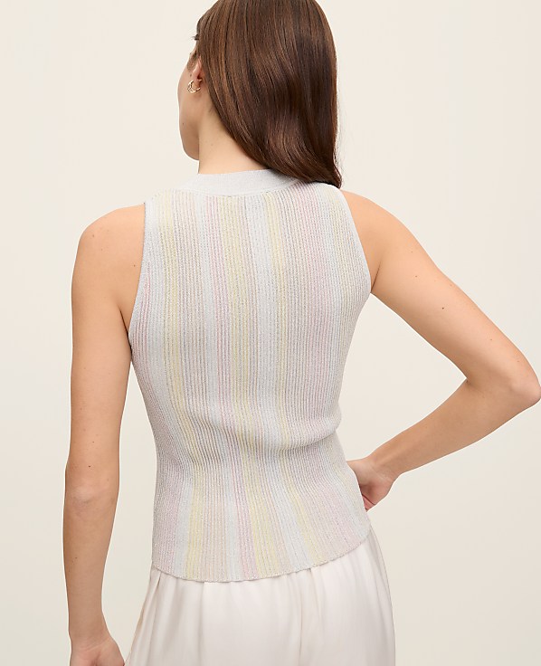 A woman wearing a sleeveless white top with vertical pleats stands against a plain light-colored background.