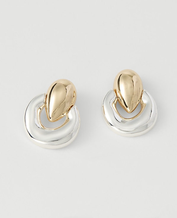 A pair of gold and silver drop earrings with a smooth, polished finish rests on a plain white background.