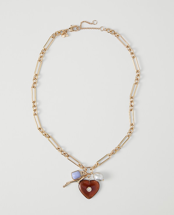A gold chain necklace with a heart-shaped pendant and charms rests on a plain white background.