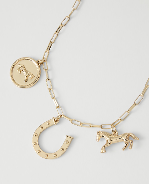 A gold necklace with horse and horseshoe charms rests on a plain white background.