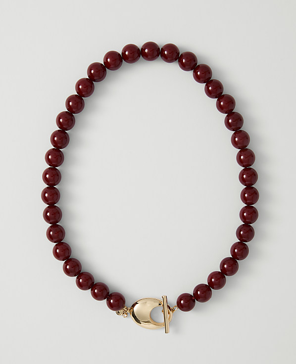 A deep red beaded necklace with a gold clasp lies on a plain white background.
