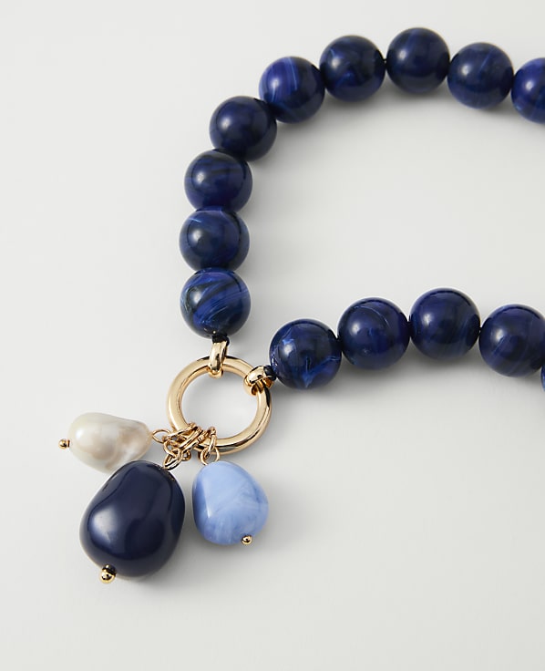 A close-up of a necklace with large blue beads and dangling charms rests on a plain white background.