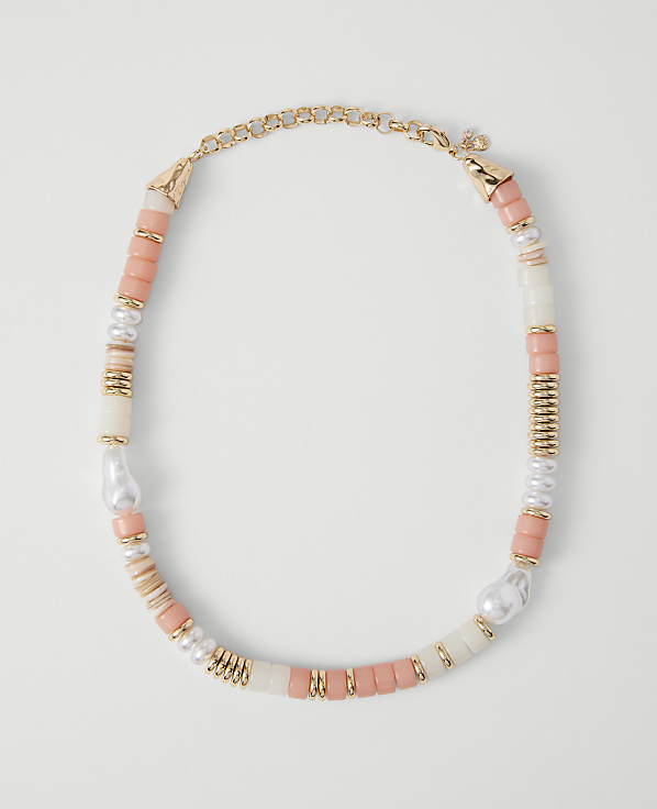 A coral, pearl, and gold beaded necklace rests on a plain white background.