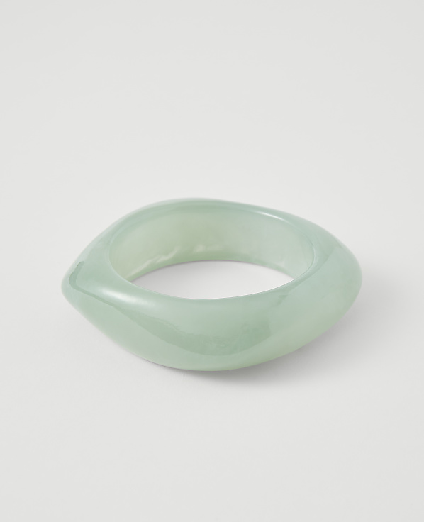 A translucent, pale green, abstractly shaped bangle rests on a plain white background.