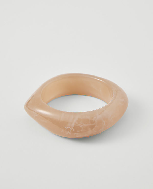 A translucent, peachy-pink bangle with a marbled pattern rests on a plain white background.