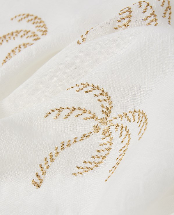 A close-up of a white fabric with embroidered golden palm trees in the foreground and background.