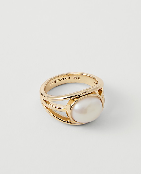 A gold ring with a large oval pearl sits on a plain white background.