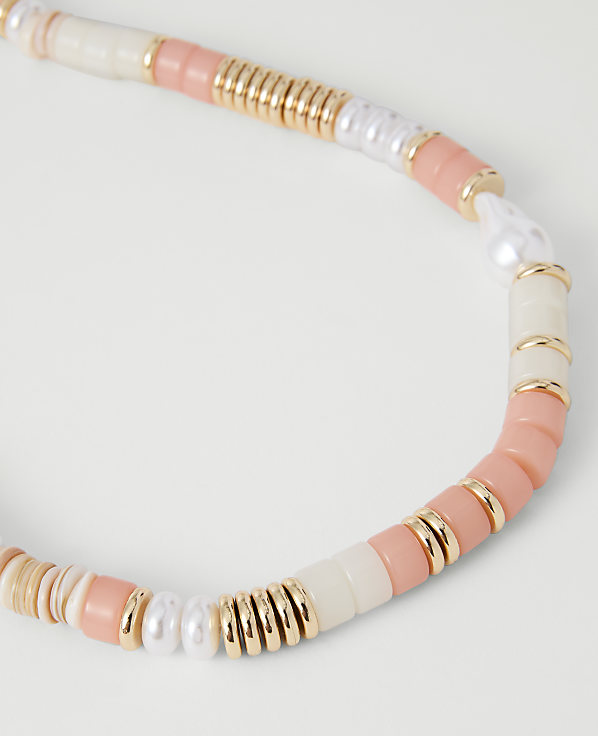 A close-up of a colorful beaded necklace with coral, white, and gold beads is set against a plain white background.
