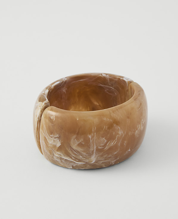 A chunky, marbled tan and white resin bangle rests on a plain white background.