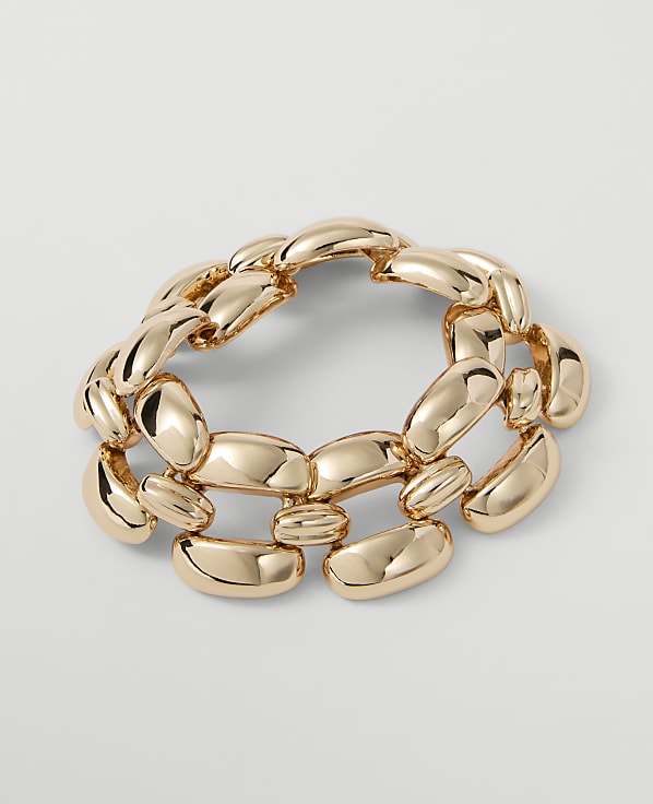 A chunky, gold-toned bracelet with oval links rests on a plain, light gray background.