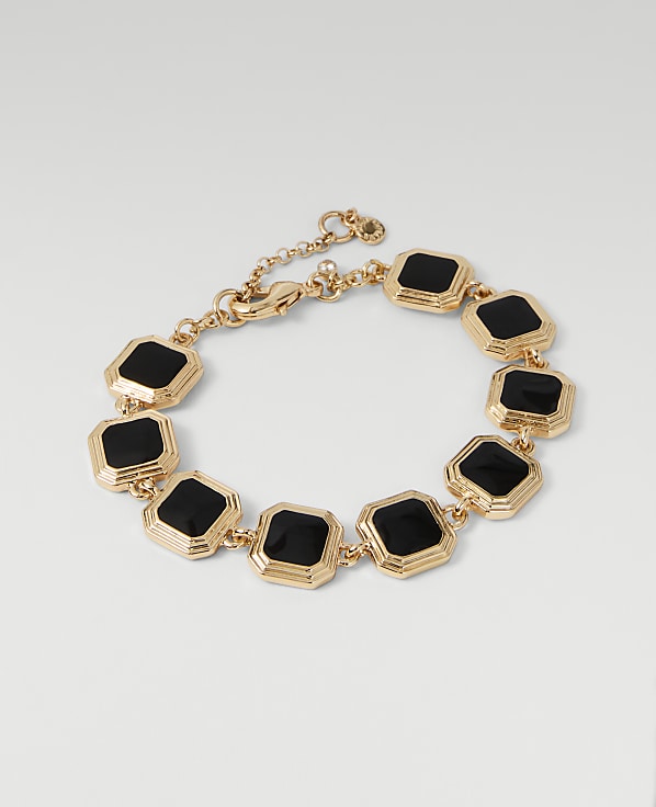 A gold bracelet with black square stones is displayed against a plain white background.
