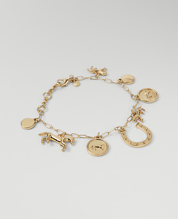 A gold charm bracelet with horse and horseshoe motifs rests on a plain, light gray background.