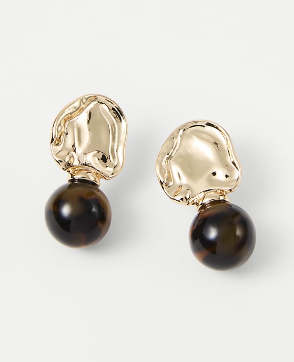 A pair of gold abstract top earrings with tortoise shell bead drops are displayed against a plain white background.