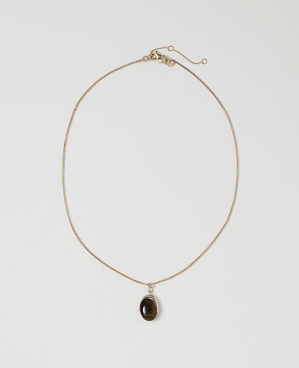 A delicate gold chain necklace with a dark oval pendant rests on a plain white background.