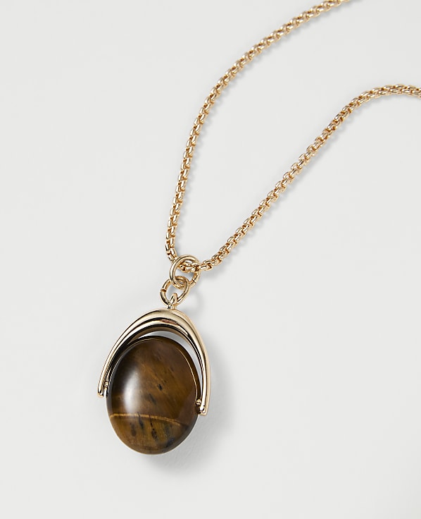 A gold chain necklace with a tiger's eye pendant hangs against a plain white background.