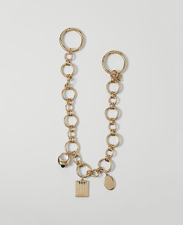 A gold chain bracelet with various charms hangs against a plain white background.