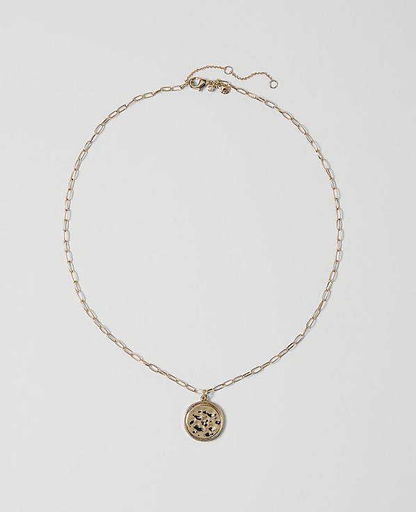 A delicate gold chain necklace with a circular pendant rests on a plain white background.