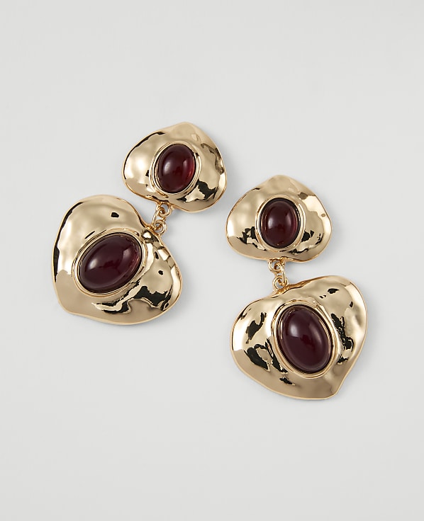 Gold heart-shaped earrings with deep red stones dangle against a plain white background.