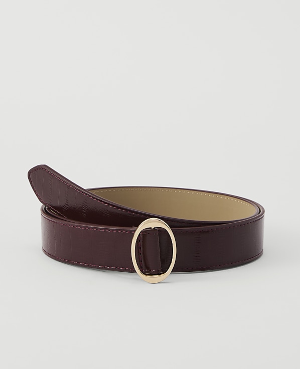 A burgundy leather belt with a gold oval buckle lies on a plain white background.