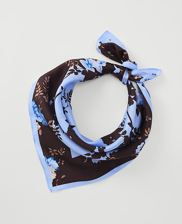 A light blue and brown floral patterned silk scarf is tied in a knot against a plain white background.