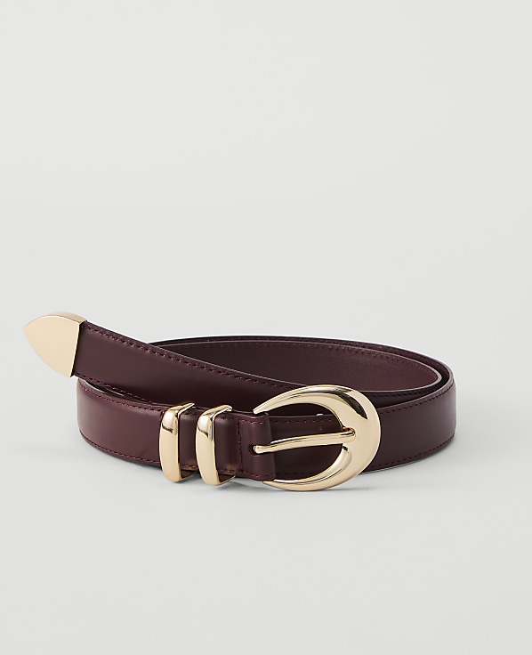 A burgundy leather belt with a gold buckle and tip rests on a plain white background.