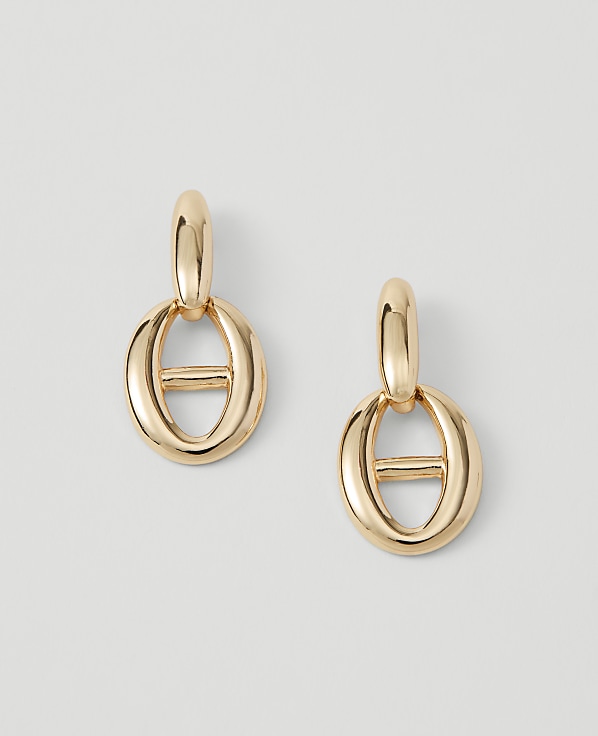 A pair of gold oval link earrings with a horizontal bar hangs against a plain white background.