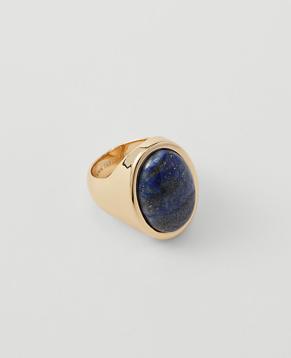 A gold signet ring with a large oval lapis lazuli stone sits on a plain white background.