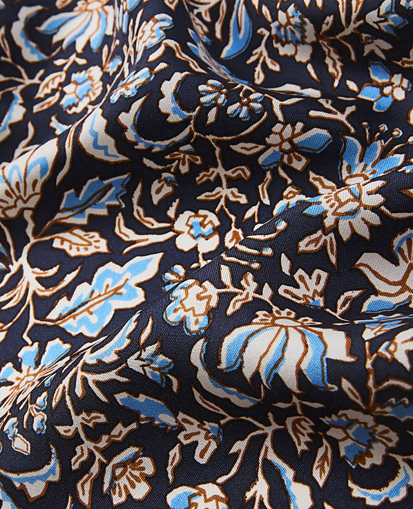 A dark blue fabric with a repeating pattern of white, light blue, and brown floral designs is draped and folded.