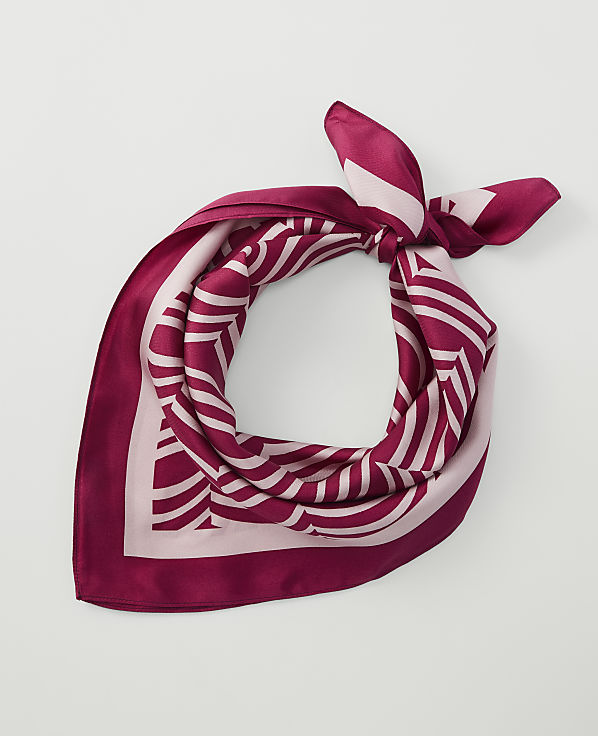 A maroon and pink patterned silk scarf is tied in a knot in the foreground against a plain white background.