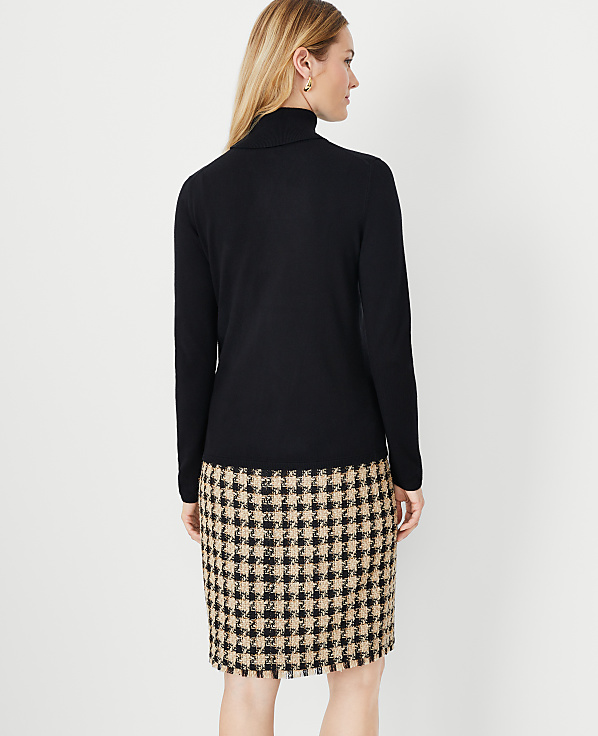 A woman in a black turtleneck and a houndstooth skirt stands against a plain white background.
