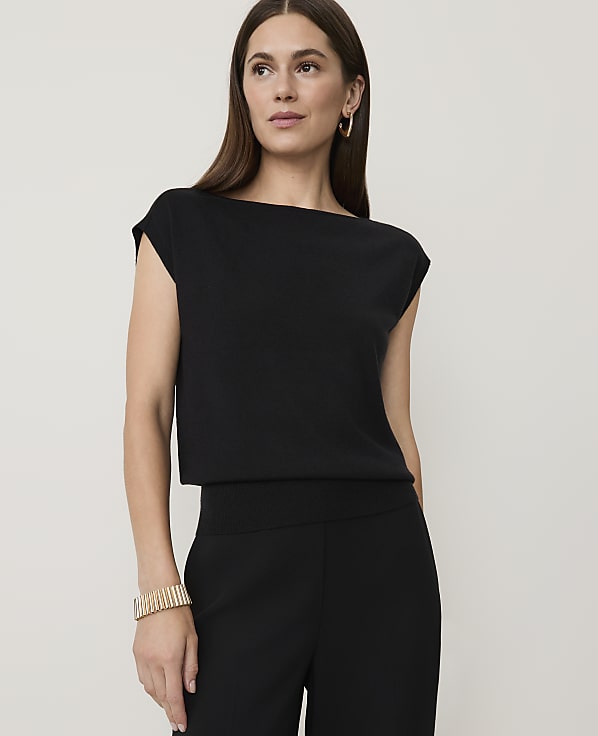 A woman in a black top and pants stands against a plain white background.