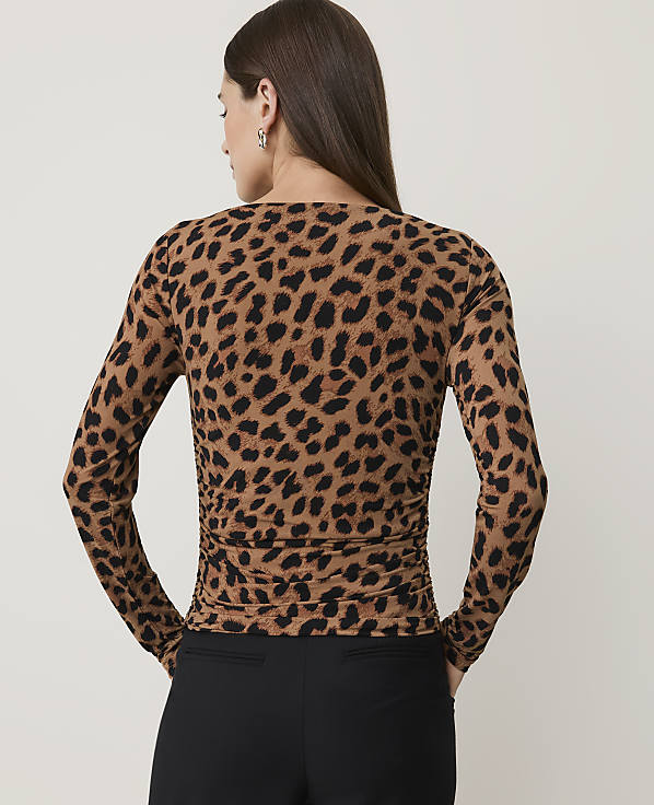 A woman in a leopard print top and black pants stands against a plain, light-colored background.