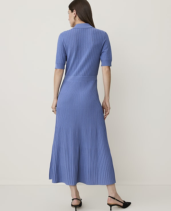A woman in a blue knit dress stands against a plain, light-colored background.