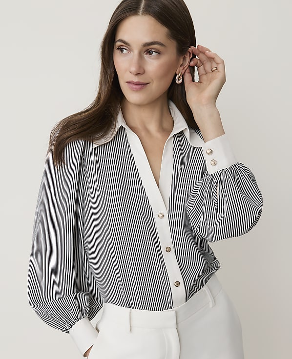 A woman in a striped blouse with puffed sleeves and white collar and cuffs poses against a plain, light background.