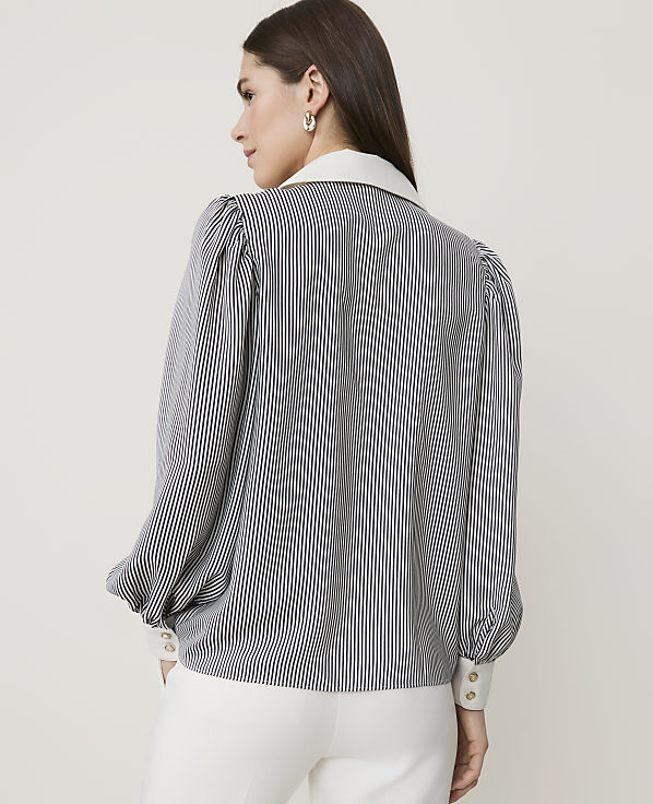 A woman in a striped blouse and white pants stands against a plain, light background.