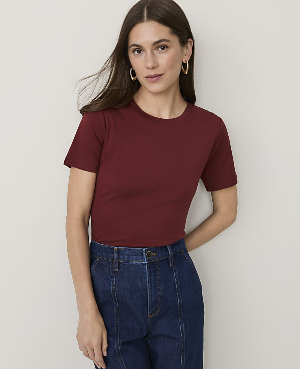 A woman in a maroon t-shirt and dark denim jeans stands against a plain white background.