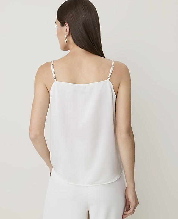 A woman in a white camisole and pants stands against a plain white background.