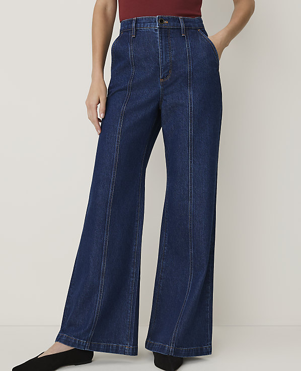 A person wearing dark wash wide-leg jeans with a maroon top stands against a plain white background.