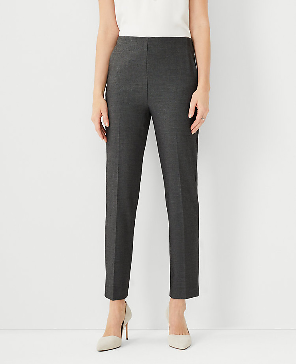 A person stands in the foreground wearing dark gray pants and light-colored heels against a plain white background.
