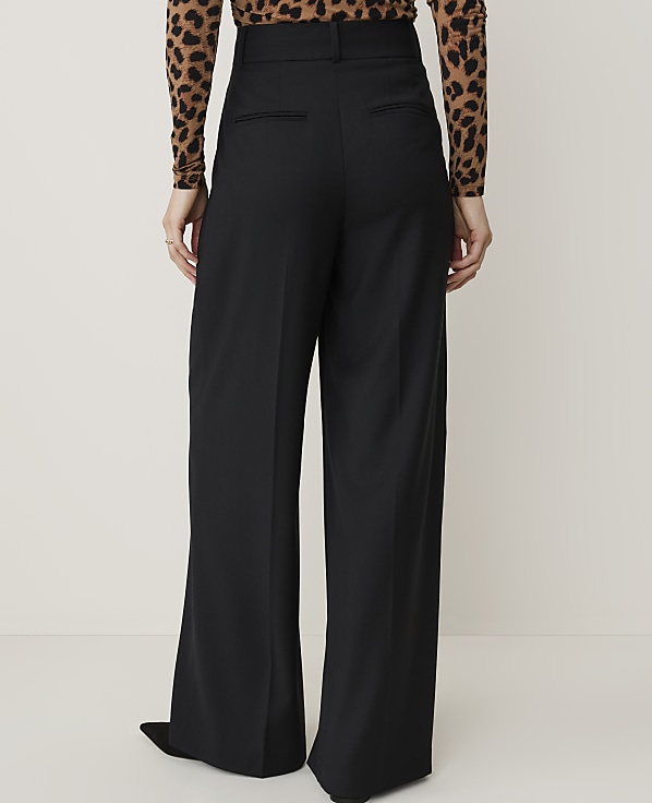 A person wearing black wide-leg pants and a leopard-print top stands against a plain, light-colored background.