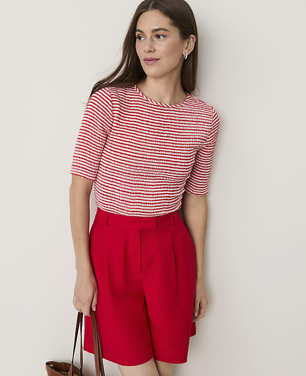 A woman in a red and white striped top and red shorts stands against a plain white background.