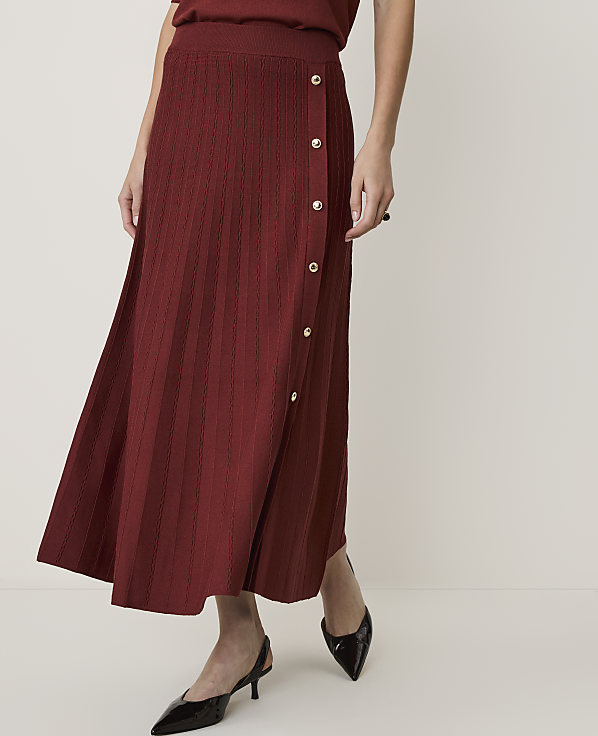 A woman in a maroon knit skirt and black heels stands against a plain white background.