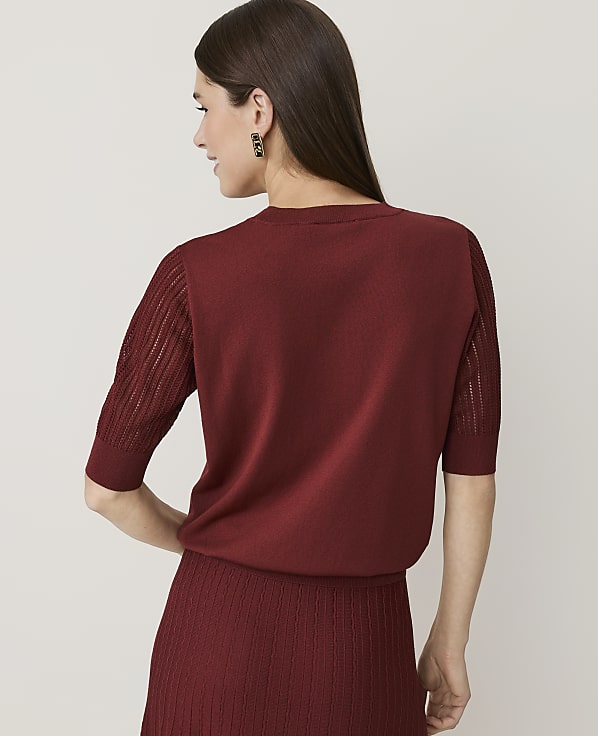 A woman in a maroon sweater and skirt stands against a plain, light-colored background.