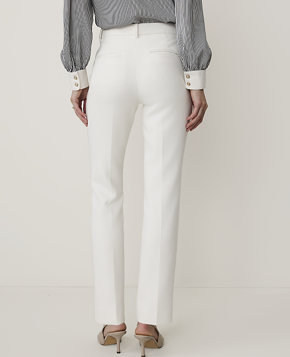 A person wearing white trousers and a striped blouse stands against a plain white background.