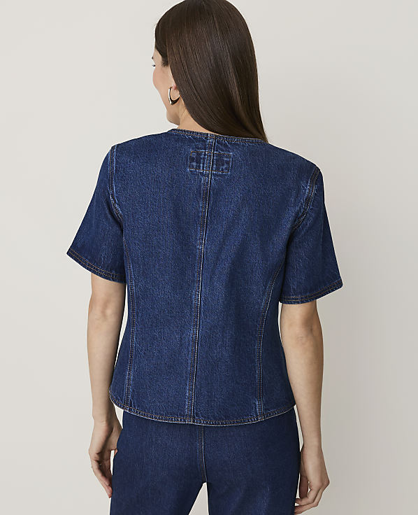 A woman in a denim top and pants stands against a plain, light-colored background.
